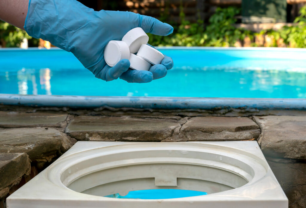 Female hand puts white tablets into pool skimmer.